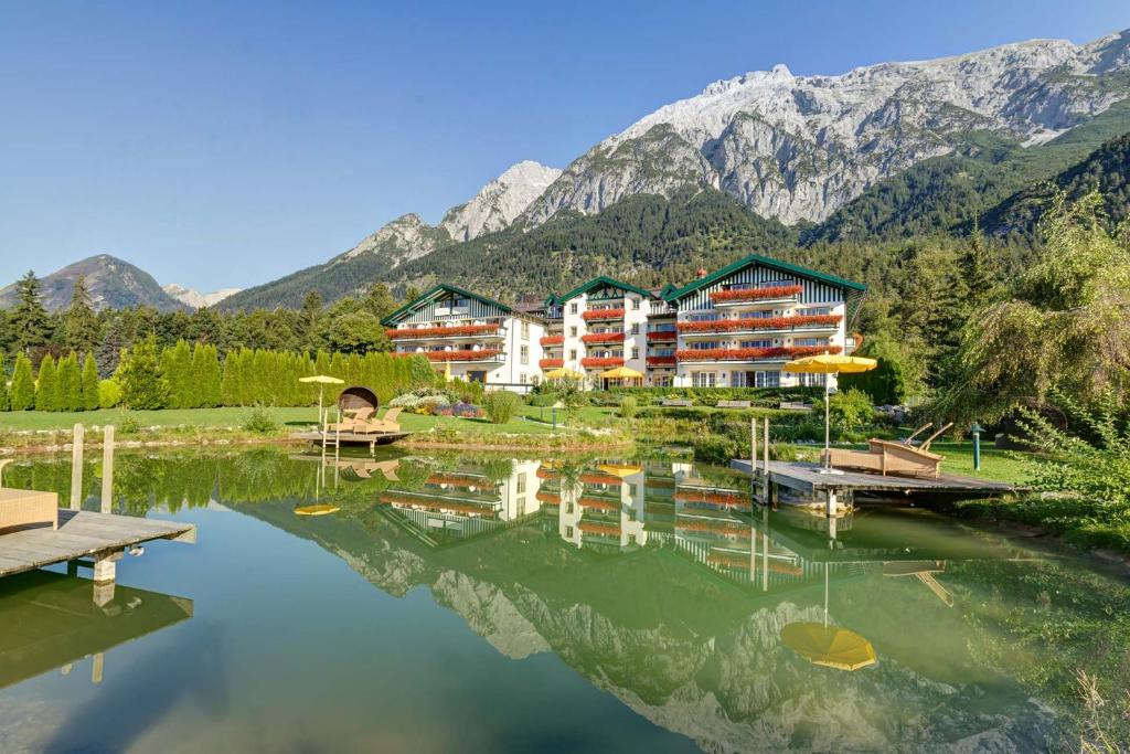 a hotel with a reflection in a lake with mountains at Alpenhotel Speckbacher Hof in Gnadenwald