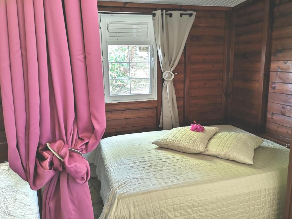 een slaapkamer met een bed met roze gordijnen en een raam bij Bungalow Maelie in La Trinité