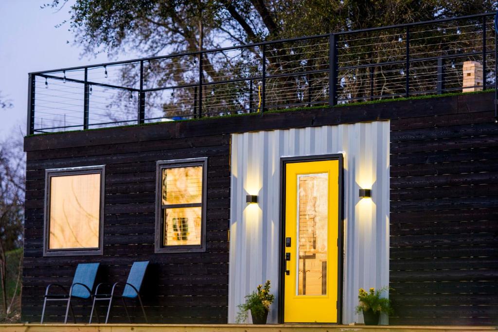 Cette petite maison dispose d'une porte jaune et d'un balcon. dans l'établissement The Zephyr Modern Luxe Container Home, à Bellmead