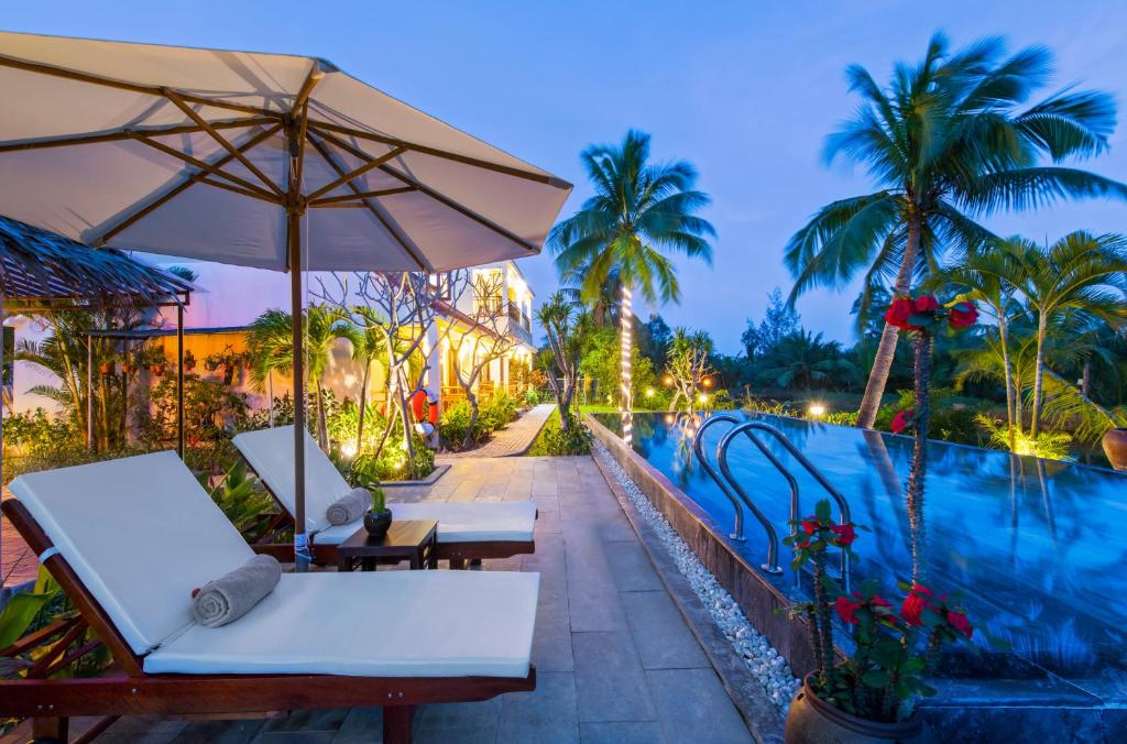 ein Sonnenschirm und Stühle neben einem Pool in der Unterkunft Pomelo Garden Boutique Villa in Hoi An