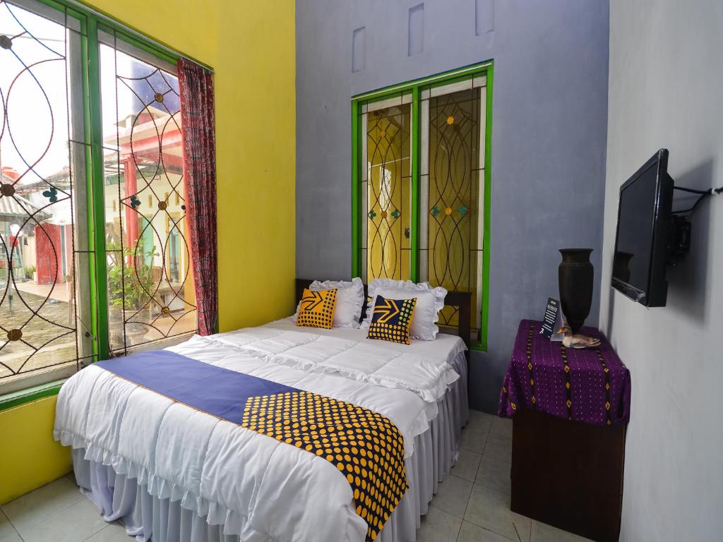 a bedroom with a bed and a tv and windows at SPOT ON 2488 Villa Tirta Melati Syariah in Banjar