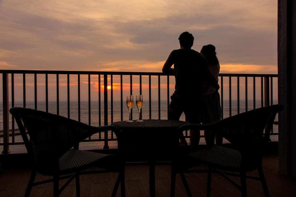 Una pareja de pie en un balcón con vistas a la puesta de sol en Meijikan en Izu
