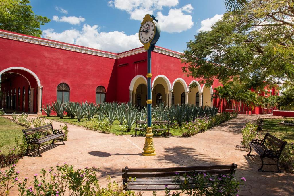 un reloj en un poste frente a un edificio rojo en Hacienda Yabucu, en Seyé
