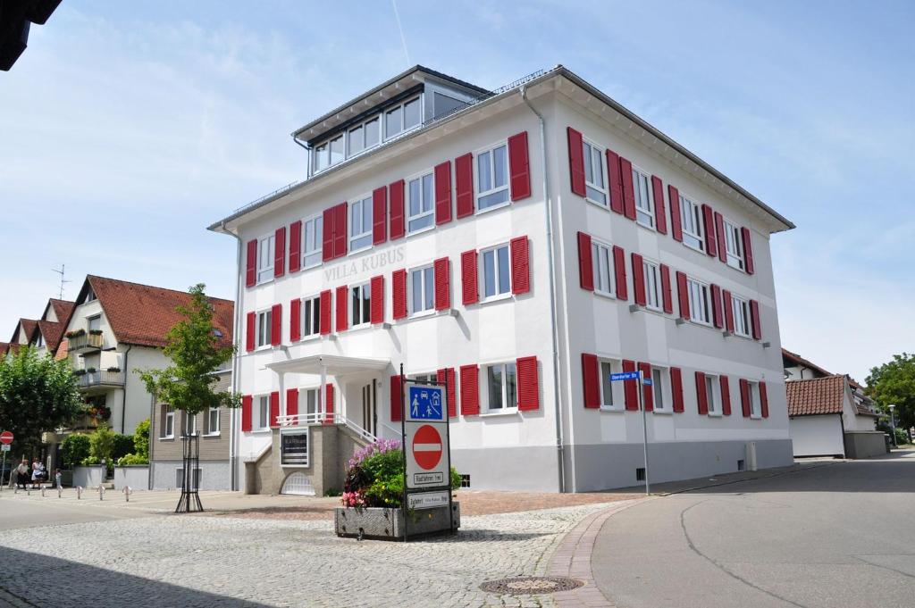 un grand bâtiment blanc avec des fenêtres rouges sur une rue dans l'établissement Villa Kubus, à Langenargen