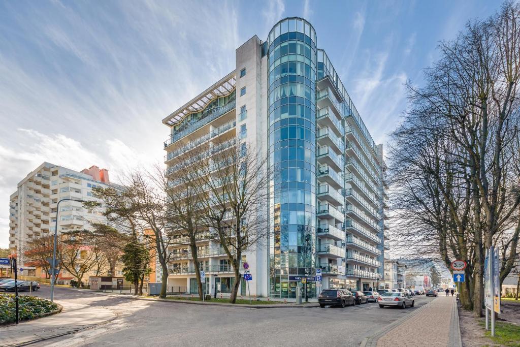 a tall glass building on a city street with cars at Apartamenty Sun & Snow Wechta - Promenada Gwiazd z sauną in Międzyzdroje