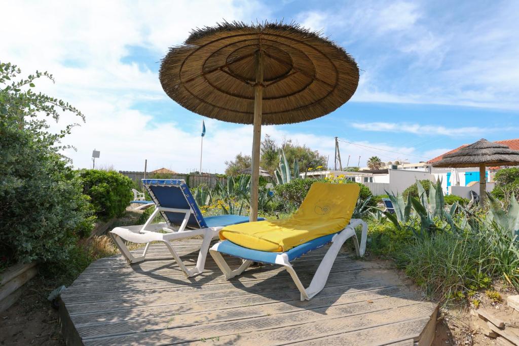2 chaises et un parasol sur une terrasse en bois dans l'établissement APPARTEMENTS ACCES PRIVE PLAGE DE LA BERGERIE, à Hyères