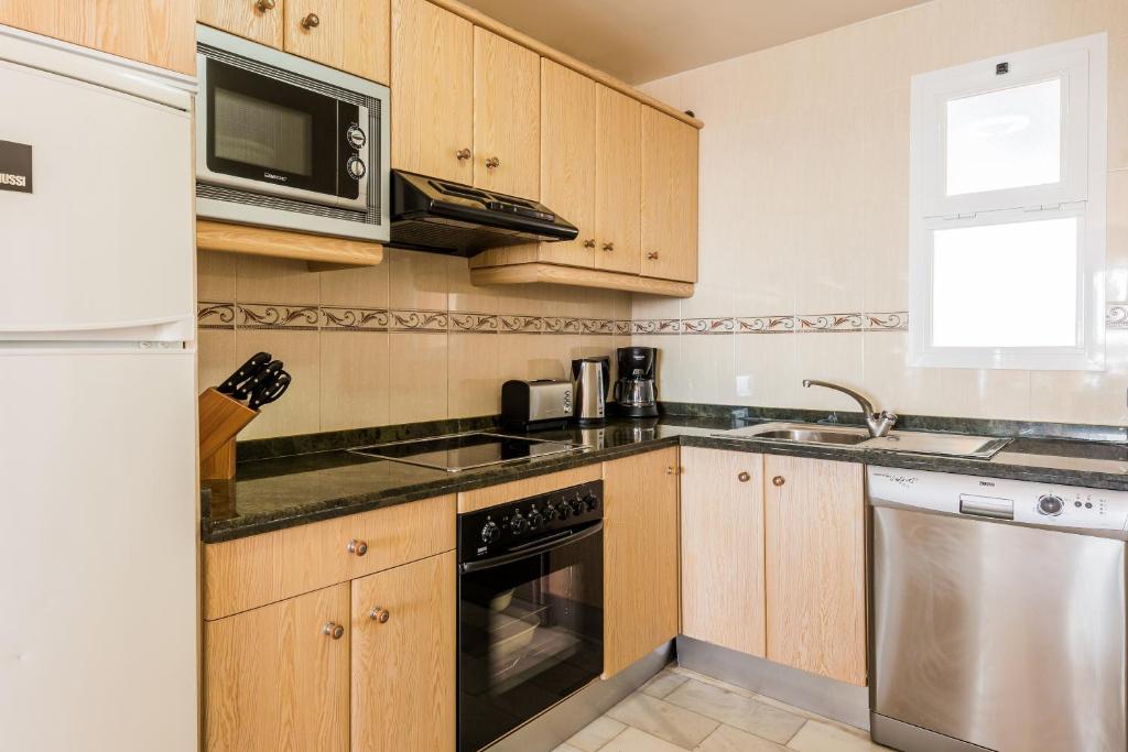 a kitchen with wooden cabinets and a microwave at Macdonald Doña Lola Resort in La Cala de Mijas