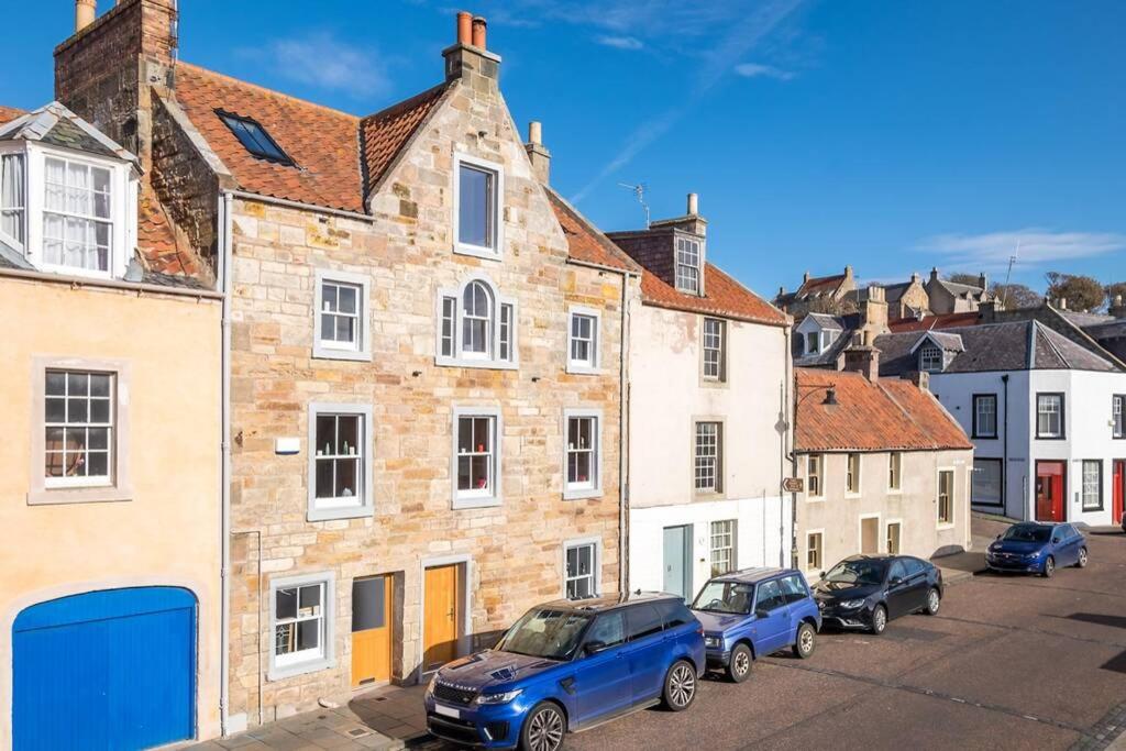 um grupo de carros estacionados num parque de estacionamento ao lado de edifícios em The Merchants House em Pittenweem