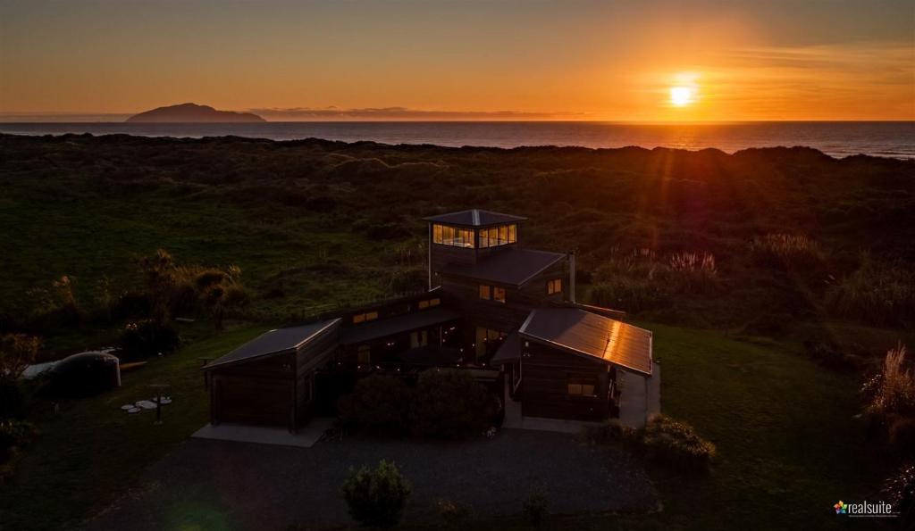 an aerial view of a house with the sunset in the background at Idyllic ocean front beach house - Waikawa Beach in Otaki Beach