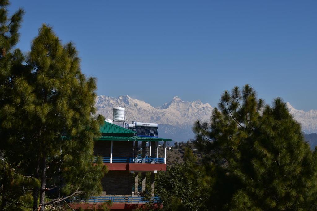 a house with a green roof with mountains in the background at Rudra Himalayan Retreat in Almora