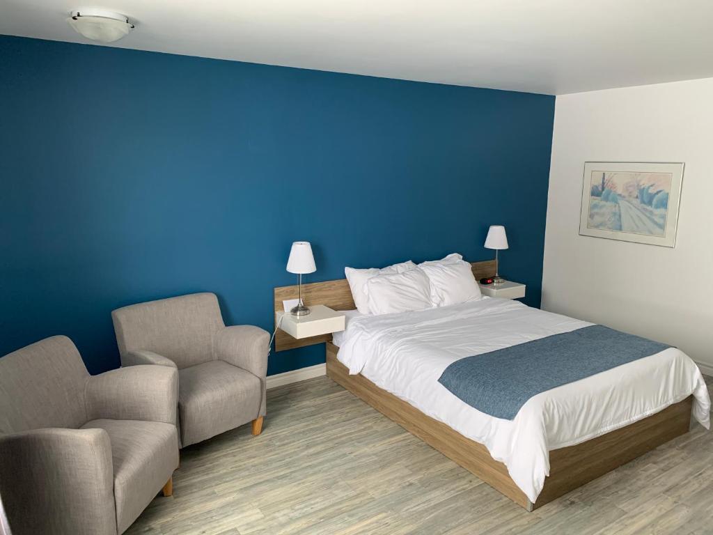 a bedroom with a blue wall and a bed and a chair at Motel Le Rond Point in Metabetchouan
