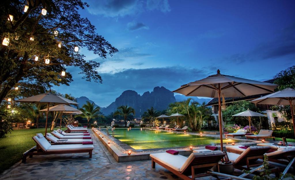 a pool with lounge chairs and umbrellas at a resort at Riverside Boutique Resort, Vang Vieng in Vang Vieng