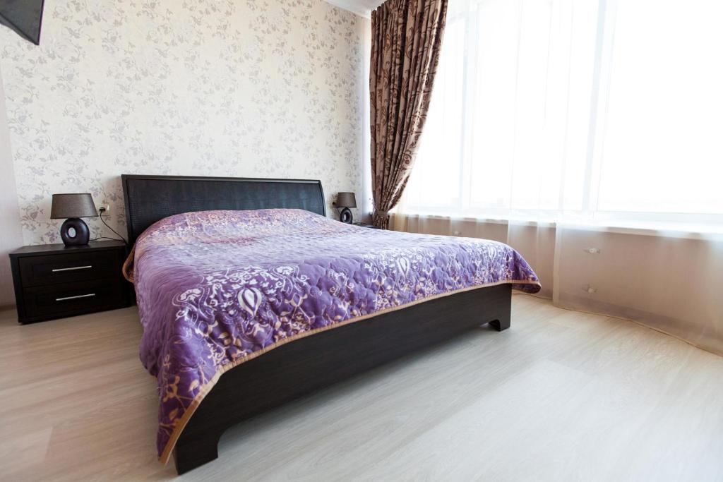 a bedroom with a bed with a purple comforter and a window at Sun City Apart Hotel in Dnipro