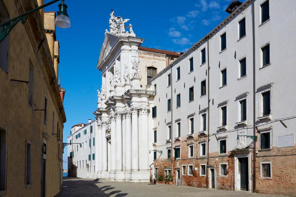 um edifício branco com uma torre de relógio numa rua em Ostello AMDG em Veneza
