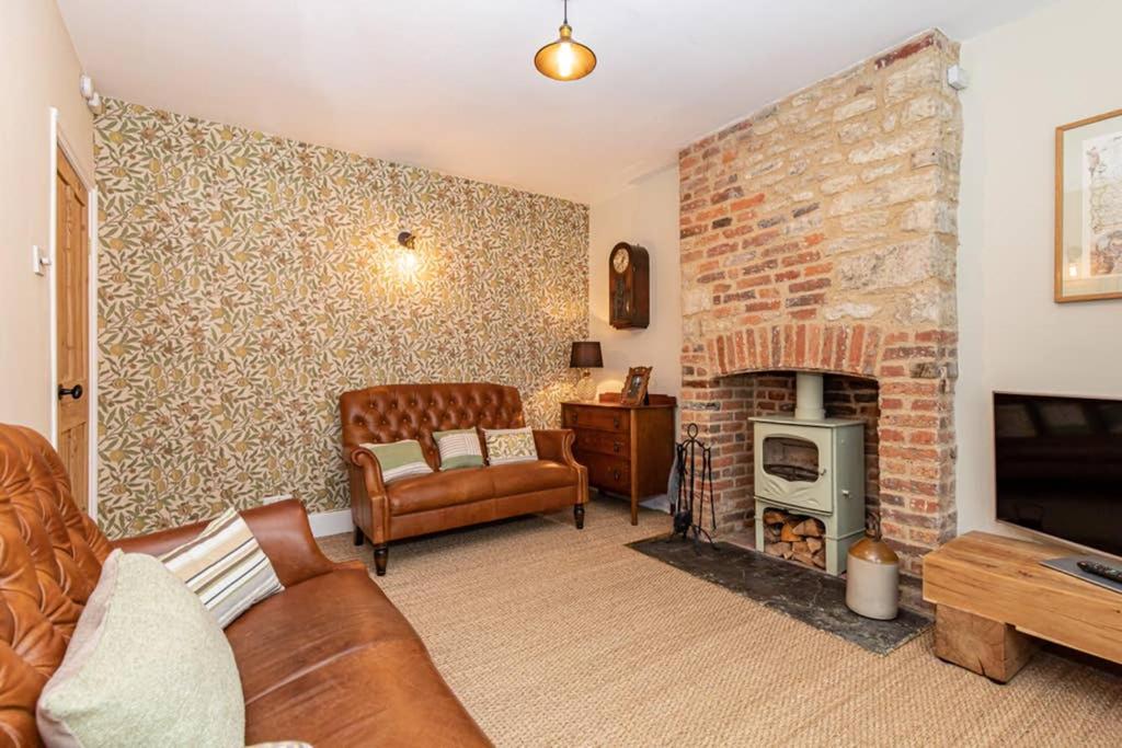 a living room with a couch and a brick fireplace at Oxfordshire Living - The Bowler Hat Cottage - Woodstock in Woodstock