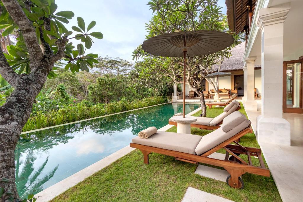 un patio al aire libre con 2 tumbonas y una sombrilla junto a la piscina en Villa Perle an Idyllic Luxury Retreat, en Karangasem