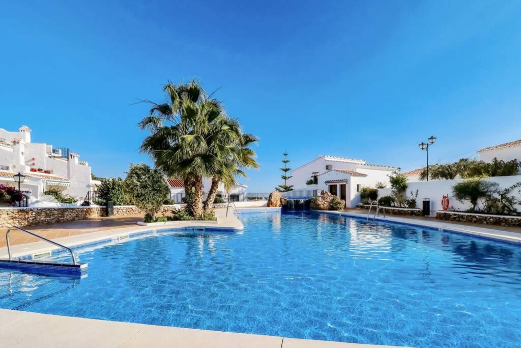 una grande piscina con una palma e edifici di Capistrano Village B, 1 bedroom + free wi-fi a Nerja