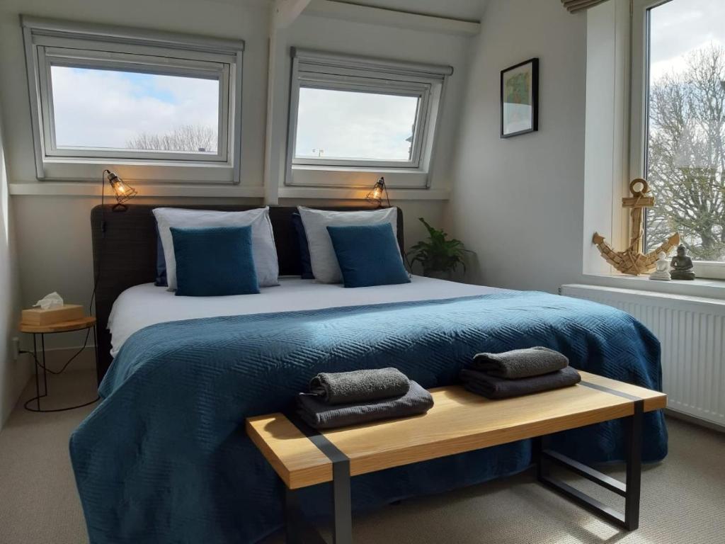 a bedroom with a large bed with blue sheets and windows at Appartement Havenzicht in Enkhuizen