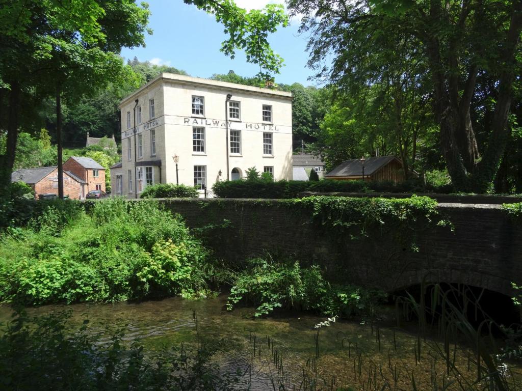 a white building next to a river with a bridge at Railway Apartments in Nailsworth