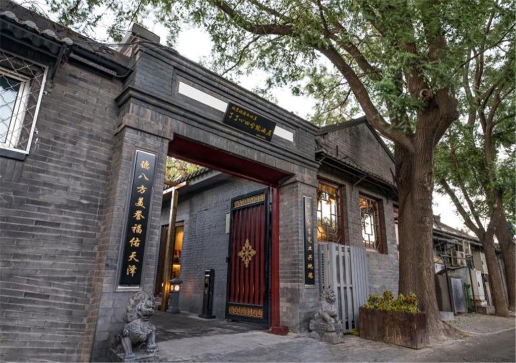 um edifício de tijolos com uma porta vermelha e uma árvore em Guipu Beihai Courtyard Hotel em Pequim