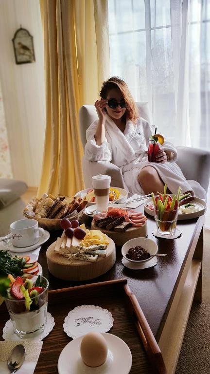 Woman in robe enjoying breakfast spread with drinks in a bright, cozy room.