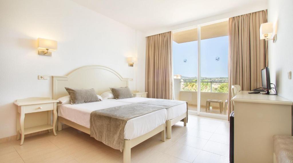 a white bedroom with a bed and a balcony at Bakour Garbi Cala Millor in Cala Millor