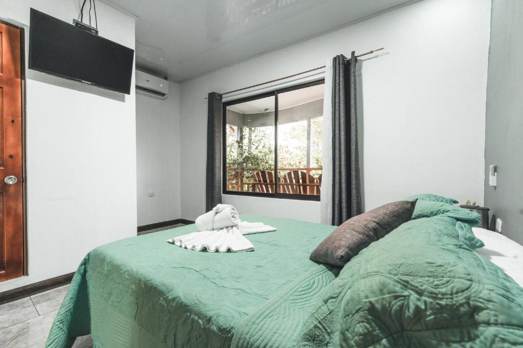 a bedroom with a bed with a green blanket and a window at Hotel Hoja de Oro Corcovado in Puerto Jiménez