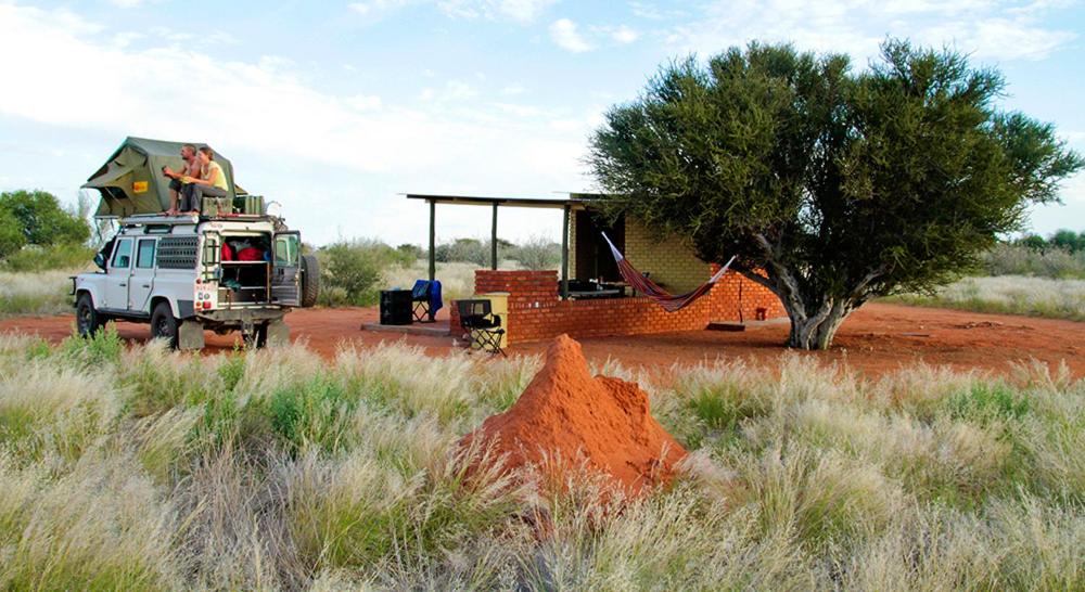 a white truck in a field with a tree and a building at Kalahari Anib Campsite in Hardap