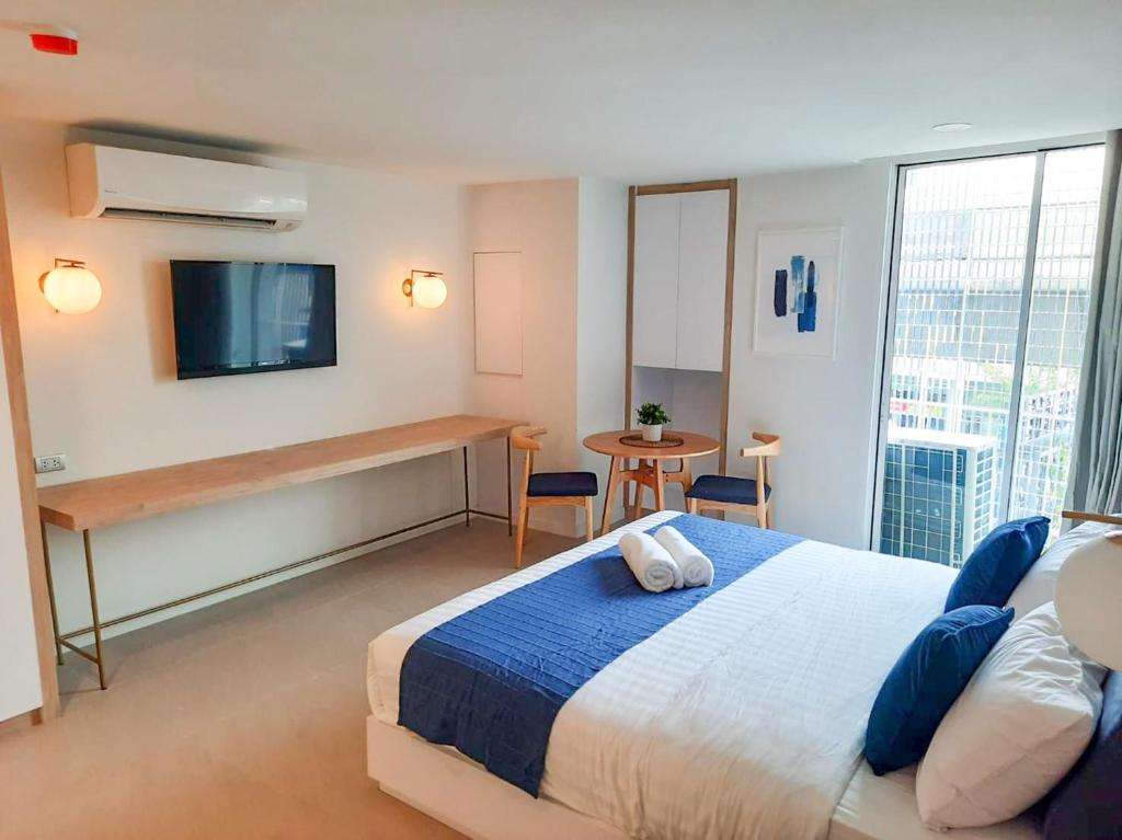 A furnished double room includes a narrow console, television, two-seat table, and large urban-facing window.