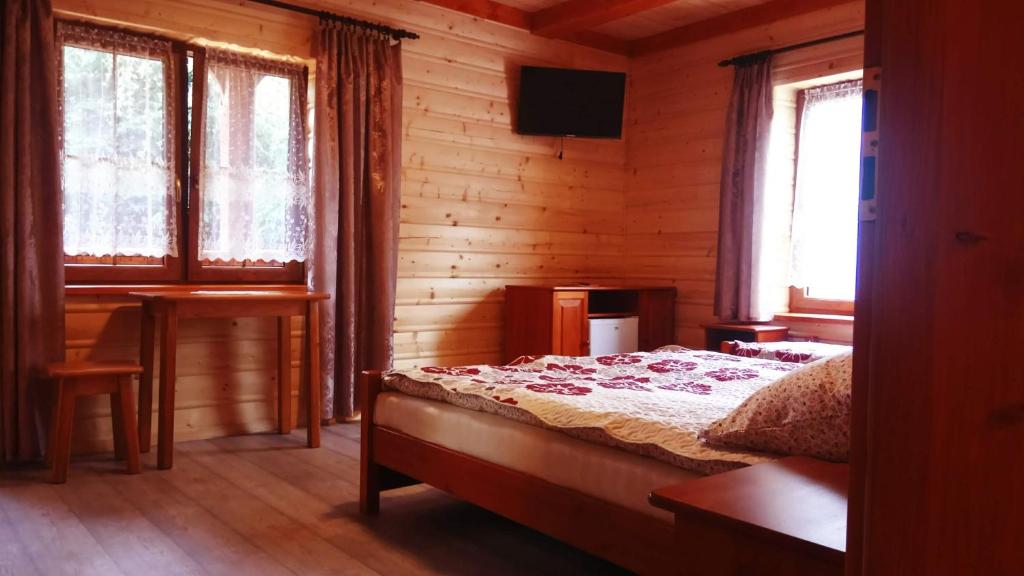 a bedroom with a bed and a desk and windows at Willa Wiktoria in Zawoja