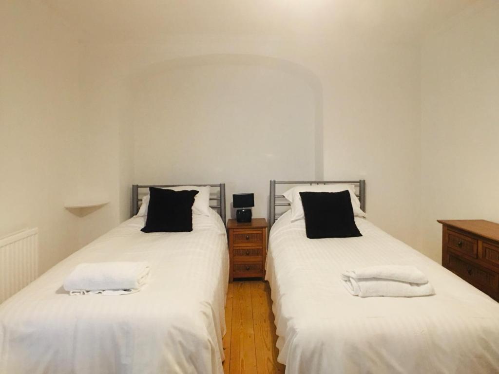 2 camas en un dormitorio con sábanas blancas y almohadas negras en MyCityHaven South Parade Mansions en Bristol