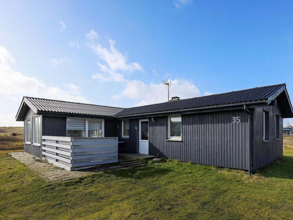 a black house on a field with a grass yard at 6 person holiday home in Lemvig in Ferring