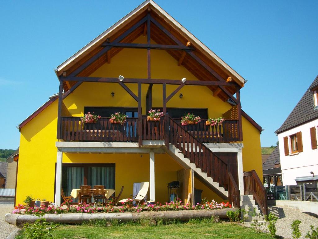 uma casa amarela com uma varanda com flores em Alsace Appartements Meyer-Krumb em Sigolsheim