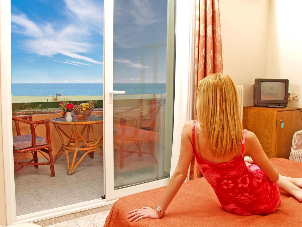 a woman in a red dress sitting on a couch in front of a window at Hotel Platon Beach in Olympiaki Akti