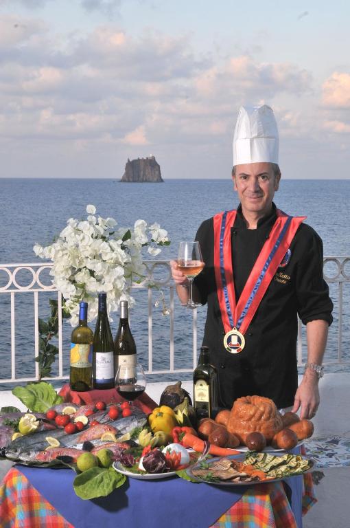 a man holding a glass of wine next to a table of food at Hotel Villaggio Stromboli - isola di Stromboli in Stromboli