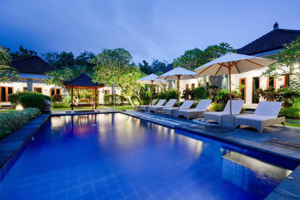 a swimming pool with lounge chairs and umbrellas at WIRA Homestay & Spa in Uluwatu