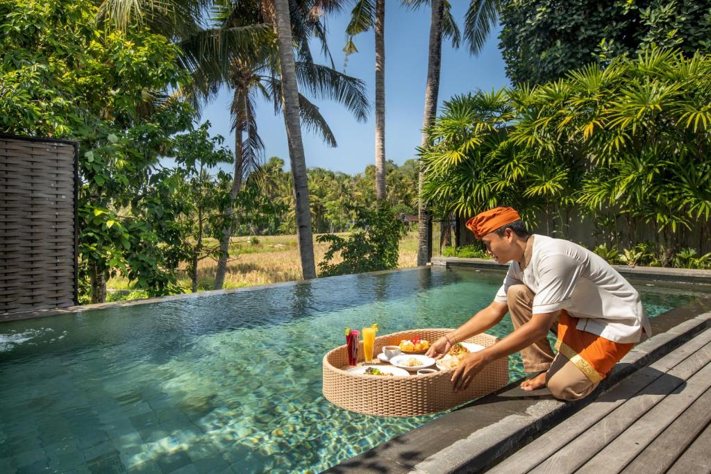 a man sitting next to a pool with a basket of food at Villa Kayu Lama in Ubud