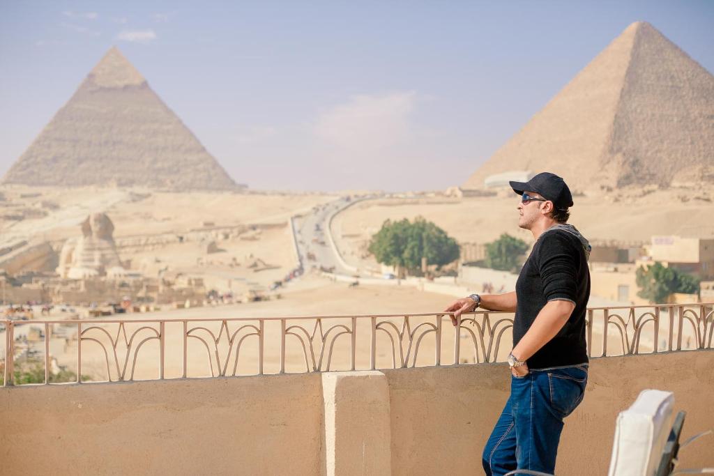 Ein Mann, der an einer Wand steht und die Pyramiden ansieht. in der Unterkunft Guardian Guest House in Kairo