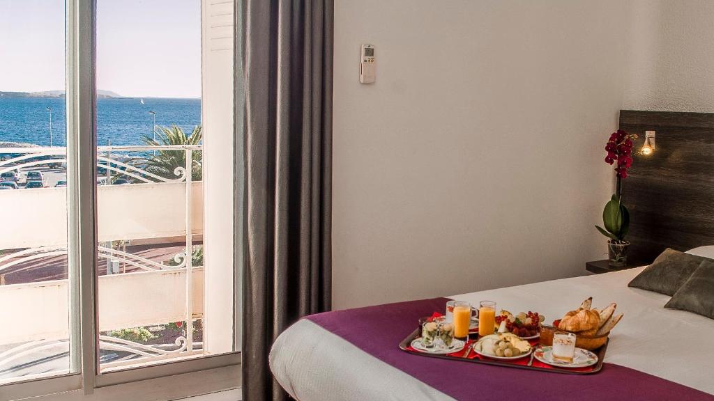 een hotelkamer met een dienblad met eten op een bed bij Hotel de la Baie in Bandol