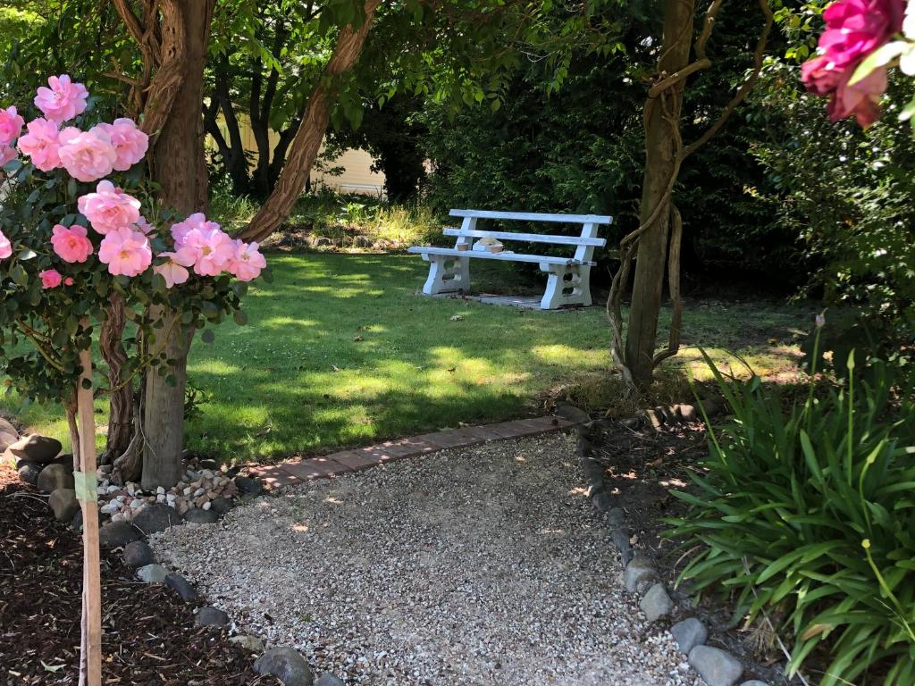 a white bench sitting in a park with pink flowers at Toolebewang Farm Cottage in Launching Place