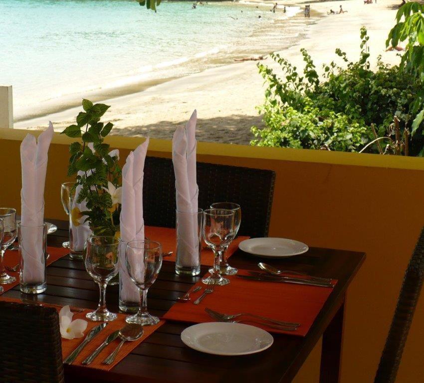 a table with plates and glasses and a view of the beach at Paradise Beach Hotel in Kingstown