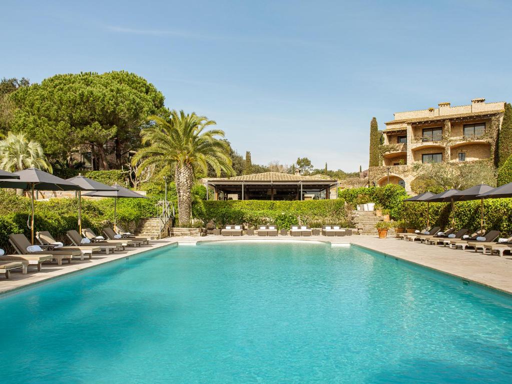 una piscina con sillas y sombrillas y un edificio en Mas de Torrent Hotel & Spa, Relais & Châteaux en Torrent