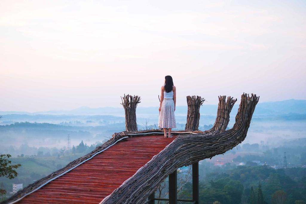 a woman standing on top of a wooden bridge looking out at the valley at Phukaew Resort & Adventure Park in Khao Kho