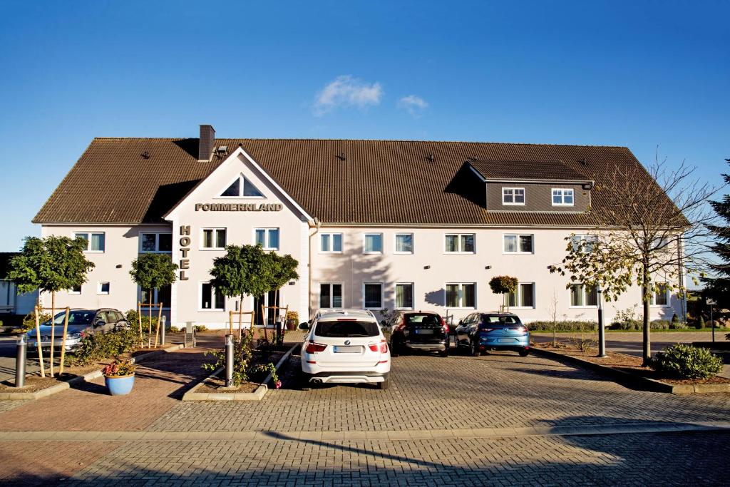 ein großes weißes Gebäude mit Autos auf einem Parkplatz in der Unterkunft Hotel Pommernland in Anklam