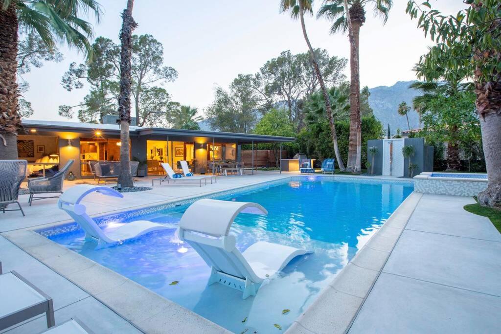 ein Pool mit zwei weißen Stühlen und ein Haus in der Unterkunft Villa Perfetto Plaza in Palm Springs