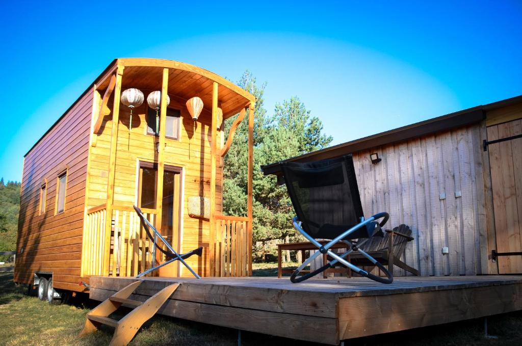 a wooden cabin with a chair on a deck at Le Petit Rias en Roulotte, 4 personnes, coin cuisine et cabinet de toilette in Saint Maurice en Chalencon