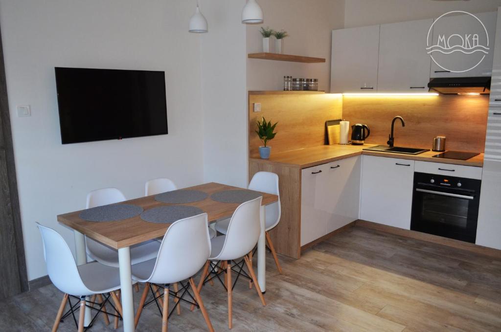 Una cocina con una mesa de madera y sillas blancas. en MoKa Apartamenty Sianożęty, en Sianożęty