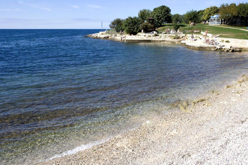 a beach with people sitting on the shore of the water at Hotel Albatros Plava Laguna in Poreč