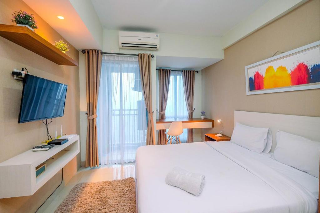 a bedroom with a large white bed and a television at Homey and Relaxing Studio @ Grand Dhika City Apartment By Travelio in Padurenan