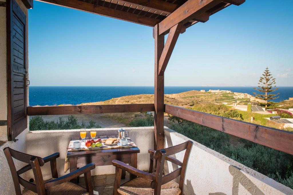 een tafel en stoelen op een balkon met uitzicht op de oceaan bij Ambelos in Agia Pelagia